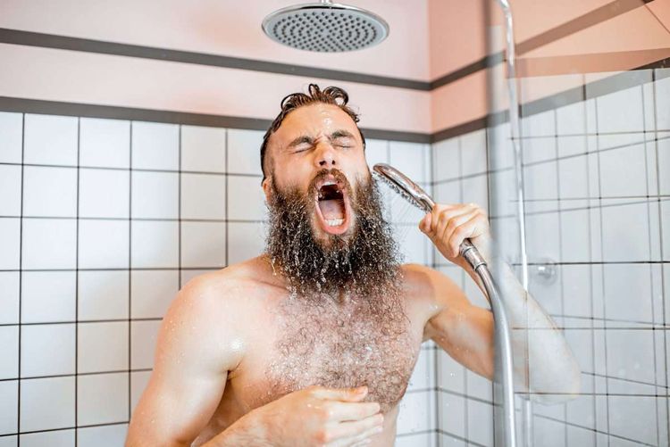 ein bärtiger Mann steht unter der Dusche, hält die Brause in der Hand und singt lauthals - sein Mund ist weit geöffnet