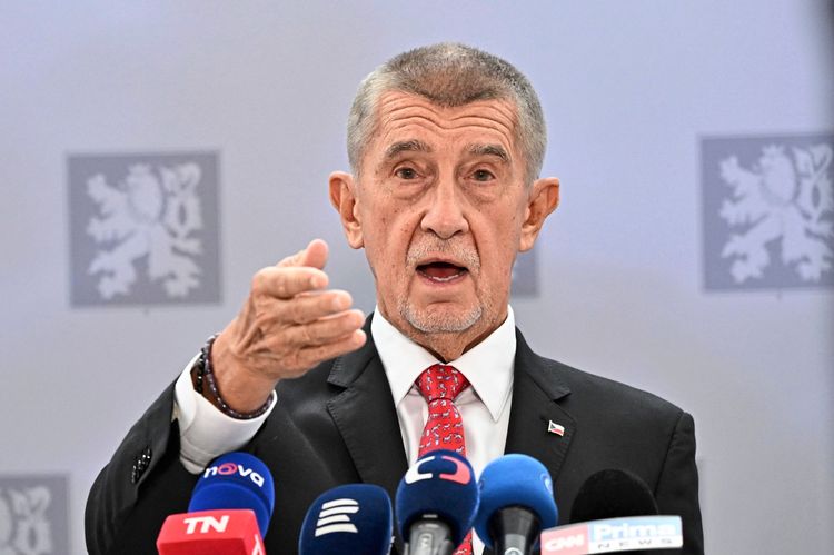 Ein Mann in Anzug und Krawatte spricht vor Mikrofonen verschiedener Medien auf einer Pressekonferenz. Im Hintergrund sind unscharfe Wappen zu sehen.