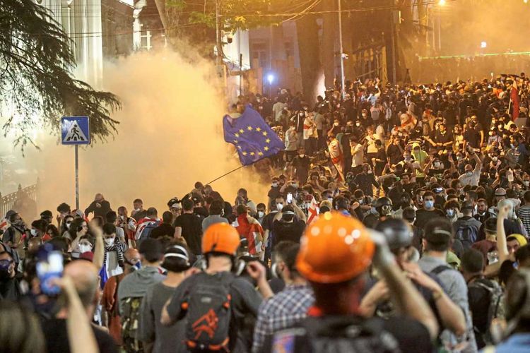 Eine Demonstration, einige Menschen tragen Bauhelme, eine große Tränengaswolke, jemand schwenkt eine EU-Fahne