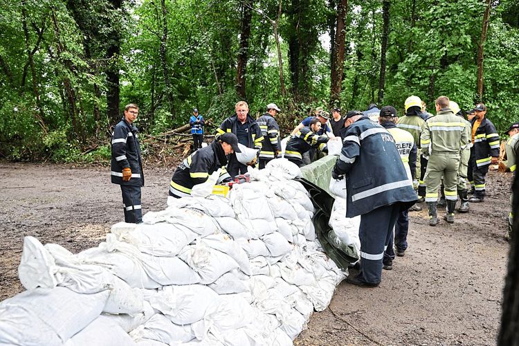 Feuerwehrleute bauen einen Schutzdamm mit Sandsäcken gegen die über die Ufer getretene Mur.