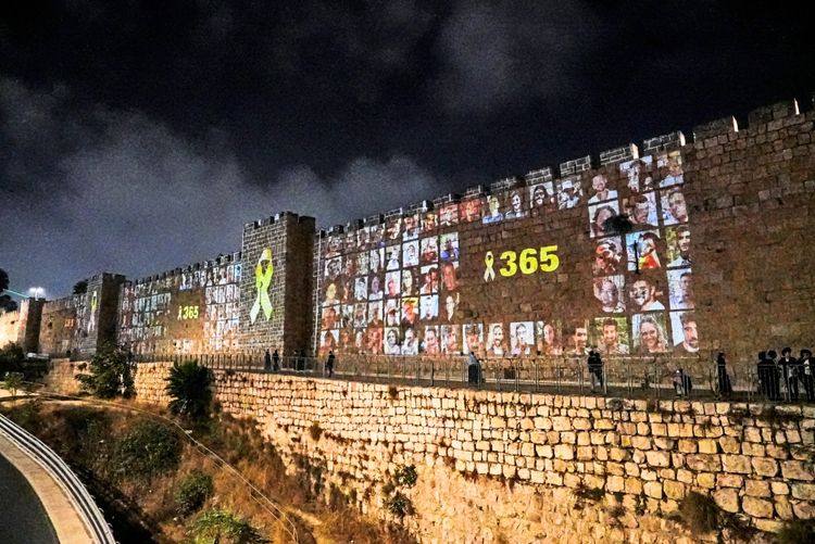 Auf die Mauern der Altstadt von Jerusalem sind bei Nacht Fotos von Geiseln projiziert, die während des Angriffs der Hamas am 7. Oktober entführt wurden. Zudem sind eine gelbe Schleife und die Zahl „365“ zu sehen. Einige Personen gehen an den Mauern entlang.