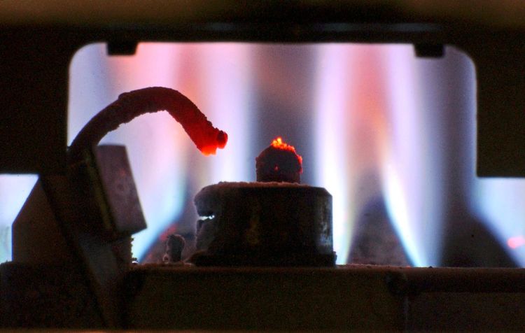 Zündvorrichtung einer Gastherme mit leuchtender Flamme in einem Haushalt, im Hintergrund blaue Gasflammen sichtbar.
