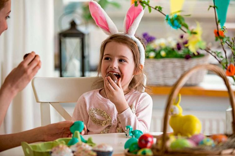 Kleines Mädchen isst ein Schokoladen-Ei und Hasenohren auf