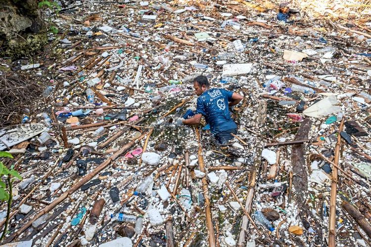 Ein Mann sammelt Plastikmüll in einem Fluss auf Bali ein.