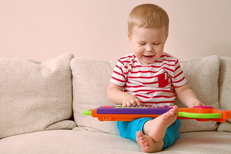 Ein Kleinkind sitzt auf einem Sofa und spielt mit einem bunten Plastikkeyboard auf seinem Schoß