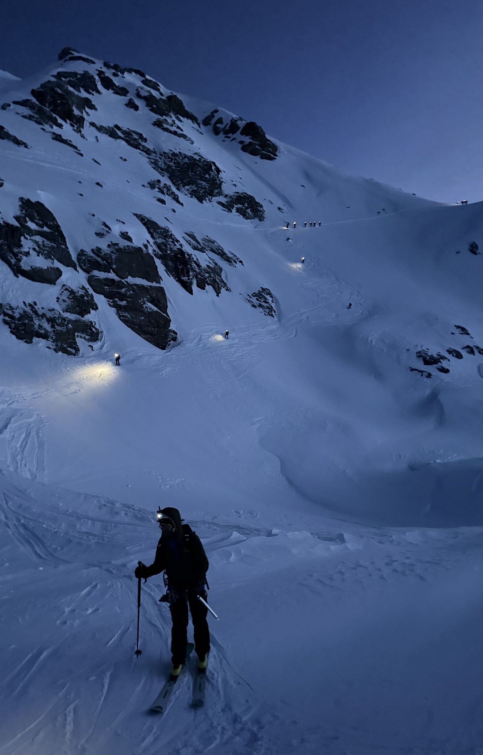 Skifahrer in der Dunkelheit mit Stirnlampen auf einem verschneiten Berg