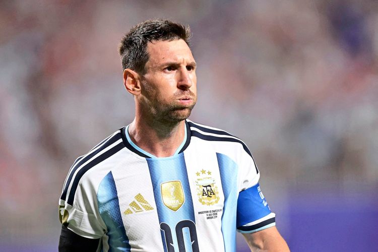 Ein Fußballspieler im Trikot der argentinischen Nationalmannschaft mit der Rückennummer 10, blau-weißen Streifen und Kapitänsbinde am linken Arm, ist auf dem Spielfeld zu sehen. Im Hintergrund verschwommene Zuschauermenge.