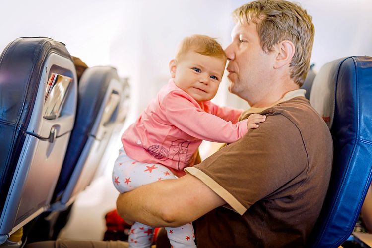 Ein Mann hält ein kleines Kind mit rosa Pulli auf dem Arm, sie sitzen in einem Flugzeug