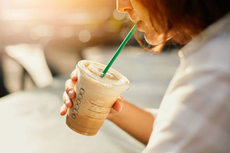Eine junge Frau trink Iced Coffe aus einem To-Go Becher aus Plastik.