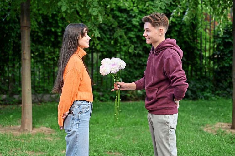 Junger Mann hält einer Freundin Blumen hin, sie ist nicht sicher, ob sie die auch annehmen möchte.