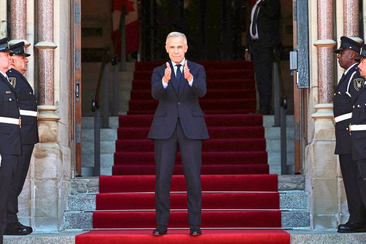 Kanadas Premier Mark Carney steht auf einem roten Teppich vor einem Gebäude mit breiter Treppe. Vier uniformierte Wachen stehen an den Seiten. Es handelt sich um eine Zeremonie in Ottawa, Kanada.