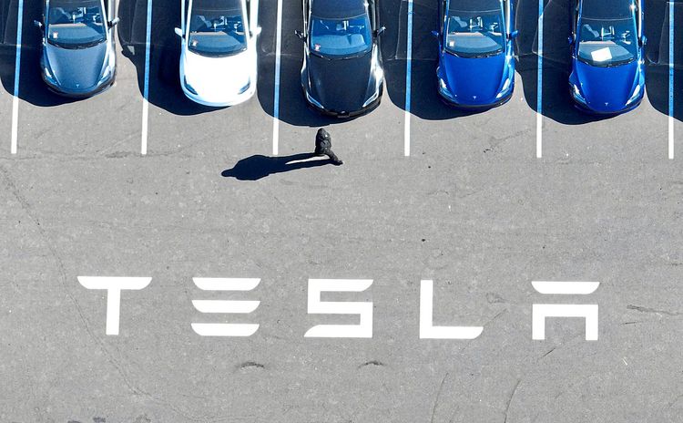 Mehrere Tesla-Autos stehen auf einem Parkplatz und ein Mensch geht daran vorbei