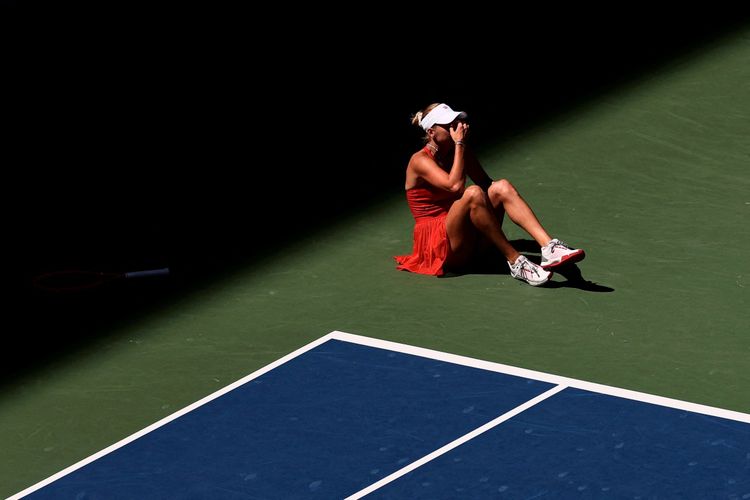Eine Tennisspielerin in einem roten Outfit sitzt auf dem Boden eines Tennisplatzes, hält sich das Gesicht und reagiert offenbar auf eine Verletzung. Der Schläger liegt in der Dunkelheit am Rand des Spielfelds.