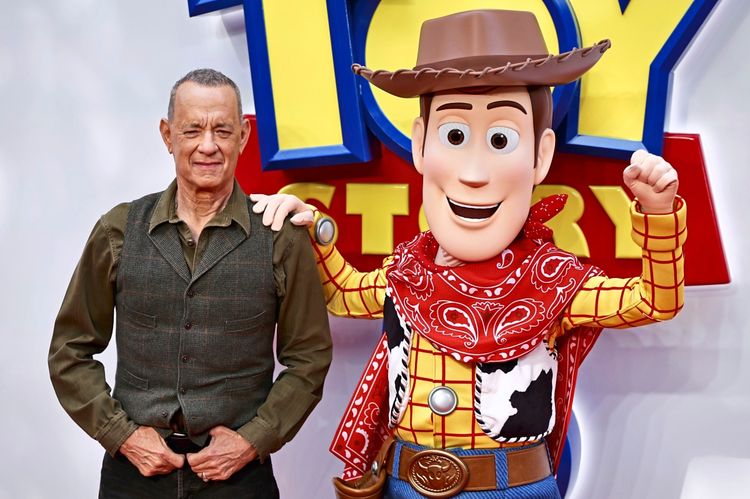 US-amerikanischer Schauspieler steht neben einer lebensgroßen Figur von Woody, einer Hauptfigur aus „Toy Story“, vor einem Hintergrund mit dem Filmtitel „Toy Story 5“. Das Bild wurde bei einem Launch-Event in London aufgenommen.