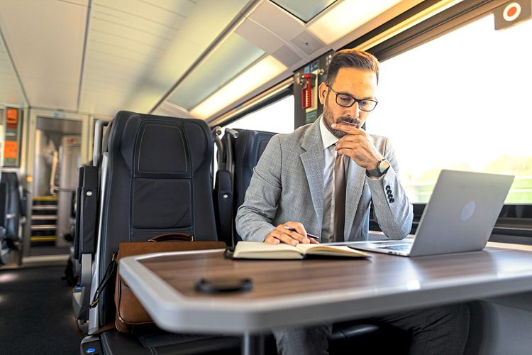 Geschäftsmann sitzt im Zug und arbeitet am Laptop.