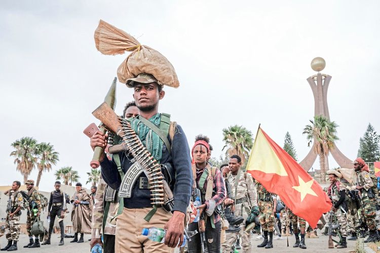 Tigray-Kämpfer der Tigray People's Liberation Front (TPLF) marschieren in Mekele, Äthiopien, am Tigray-Märtyrer-Denkmal. Eine Person trägt ein Gewehr und Munition, andere halten eine TPLF-Flagge. Im Hintergrund sind weitere Kämpfer und Palmen erkennbar.