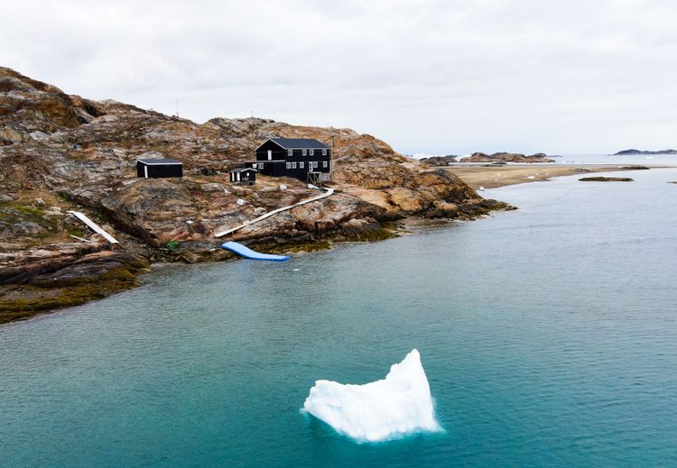 Österreichische Polarforschungsstation Grönland, ein zweistöckiges schwarzes Gebäude am Rande eines Fjords, im Vordergrund schwimmt ein Eisberg