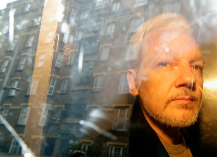 Der Whistleblower Julian Assange blickt 2019 nach einem Gerichtstermin in London aus einem Fenster, darin spiegeln sich Häuserfassaden.