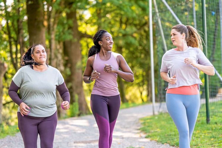 Drei Frauen mit unterschiedlichen Körpertypen laufen im Park und unterhalten sich dabei 