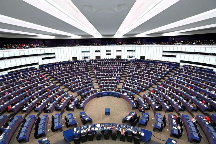 Blick in den großen EU-Sitzungssaal. Blaue Tische und Stühle. Viele Menschen sitzen und haben weiße Blätter vor sich.