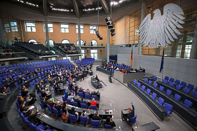 Blick in Bundestag. Blaue Sitze. Großer Bundesadler. Einige Abgeordnete heben die Hand. 
