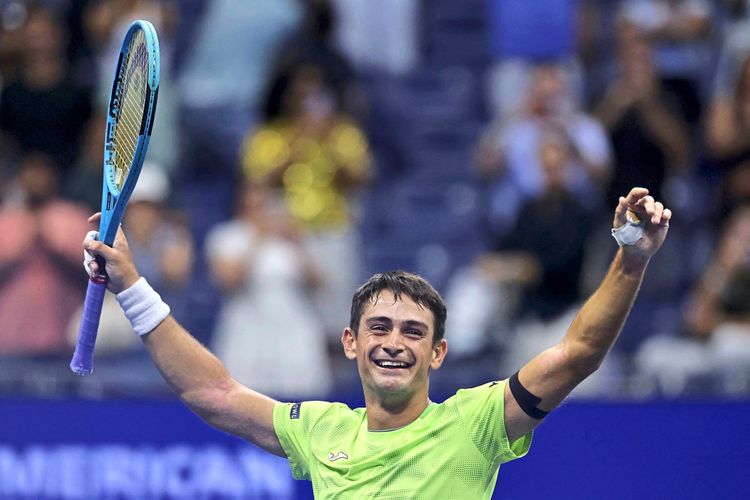 Ein Tennisspieler in einem neongrünen Shirt jubelt mit einem Tennisschläger in der Hand, während das Publikum im Hintergrund applaudiert.