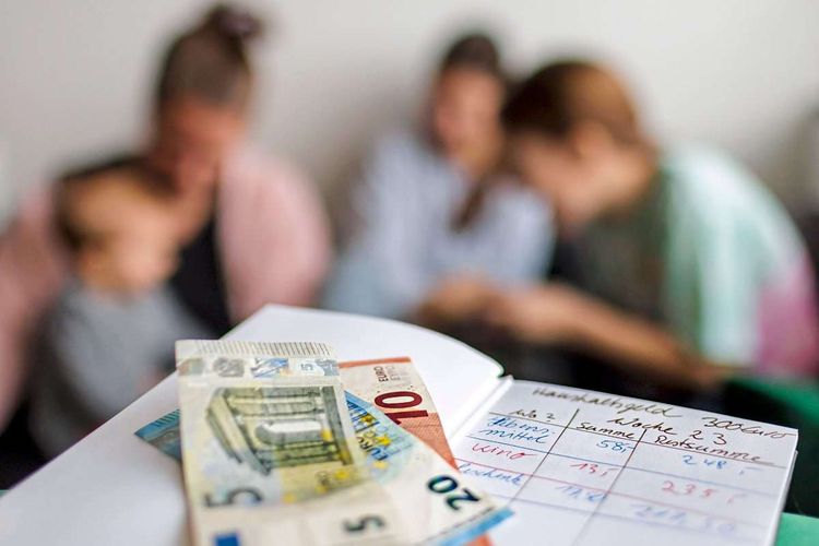 Haushaltsbuch mit fuenfunddreissig Euro. Im Hintergrund eine Mutter mit drei Kindern. Bonn Deutschland *** Household boo