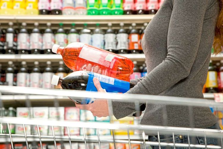 Frau vergleicht im Supermarkt zwei Flaschen Limonaden miteinander