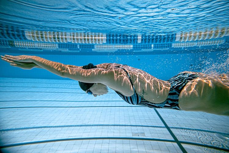 Frau schwimmt unter Wasser in einem Hallenbad.