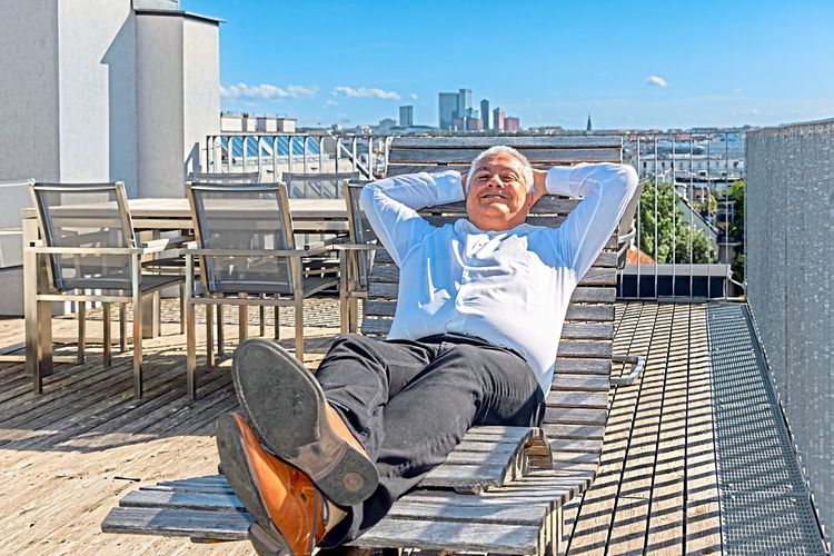 Der Berater Mario Filoxenidis auf der Terrasse seines Büros, in einem Liegestuhl liegend, hinter ihm die Skyline des Wienerbergs.