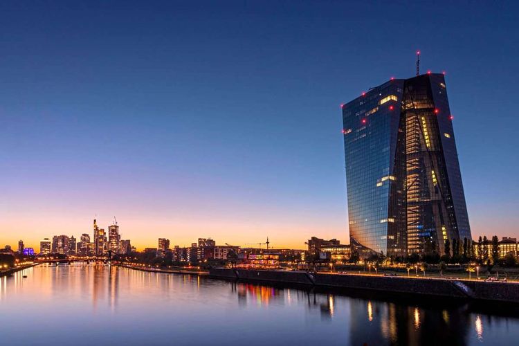 Die Europäische Zentralbank EZB und die Frankfurter Bankenskyline spiegeln sich nach Sonnenuntergang im Main.
