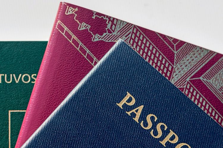 Drei Pässe in Nahaufnahme: ein blauer Pass mit der goldenen Aufschrift 
