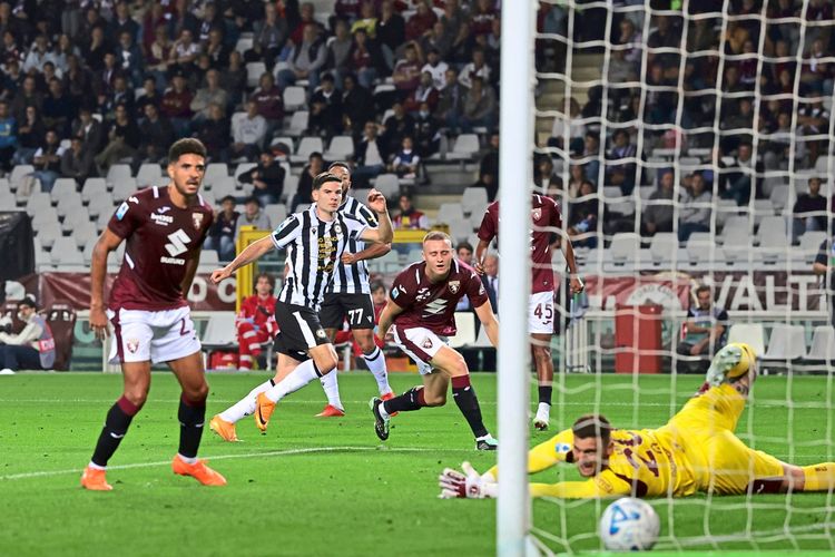 Ein Moment während eines Fußballspiels zwischen Torino FC und Udinese Calcio in der Serie A. Ein Spieler von Udinese schießt ein Tor, während der Torhüter von Torino auf dem Boden liegt. Im Hintergrund sind Zuschauer und andere Spieler zu sehen.