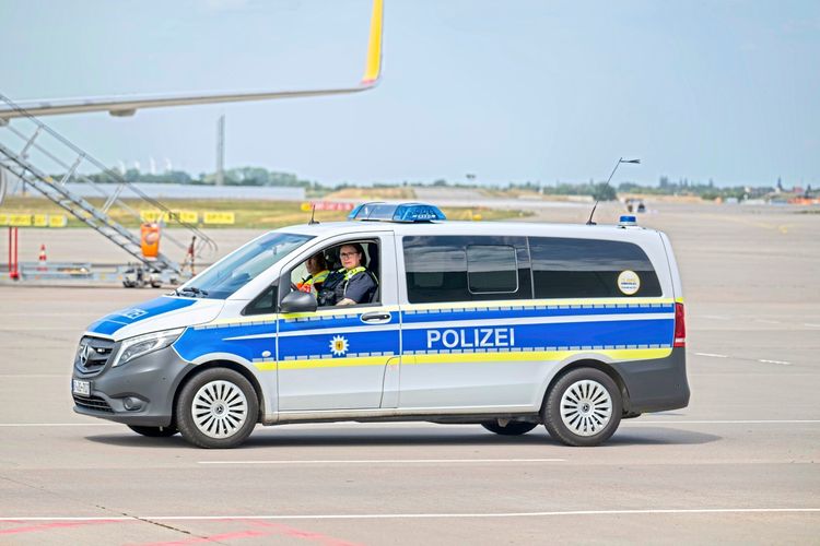 Ein Polizeifahrzeug mit der Aufschrift „Polizei“ steht auf dem Gelände des Flughafens Leipzig/Halle. Im Hintergrund sind Flugzeugtreppen und Teile eines Flugzeugs zu sehen.