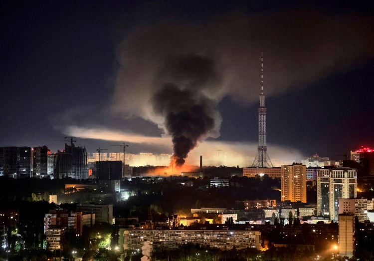 Rauch steigt über einer beleuchteten Stadt bei Nacht auf, verursacht durch einen Brand nach einem Raketenangriff. Im Hintergrund ist ein großer Sendeturm zu sehen.