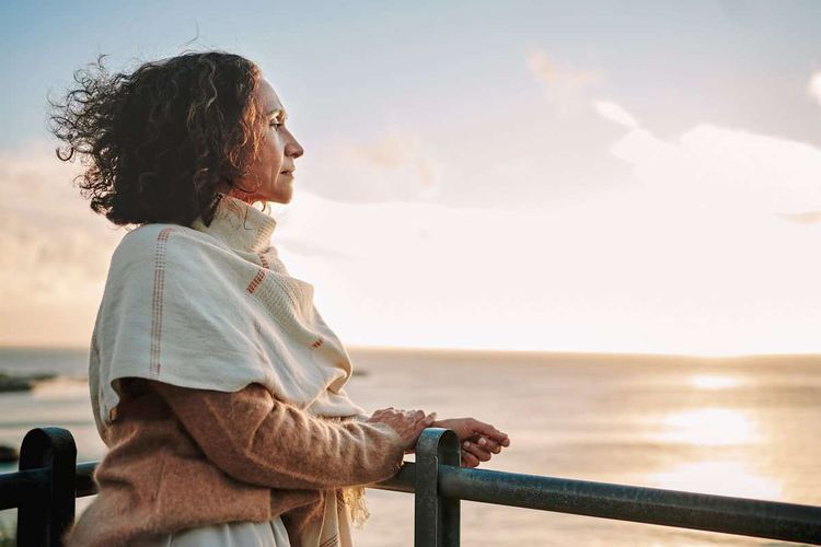 Frau lehnt an einem Geländer und blickt nachdenklich zum Sonnenuntergang auf dem Meer 
