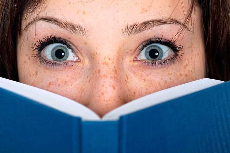 Eine Frau schaut mit weit aufgerissenen Augen hinter einem Buch hervor