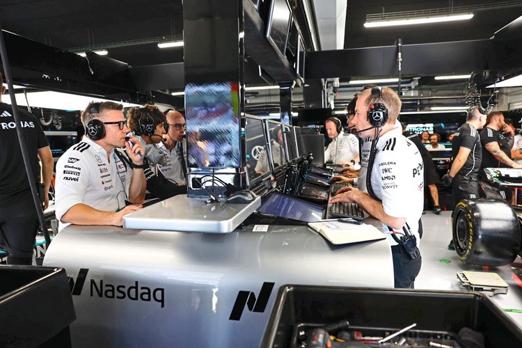 Mehrere Teammitglieder des Mercedes-AMG Petronas F1 Teams arbeiten in der Box des Teams während des Formel-1-Grand-Prix von Spanien 2025 am Circuit de Barcelona-Catalunya. Sie tragen Headsets, arbeiten an Computern und überwachen die Rennaktivitäten. Im Hintergrund sind weitere Teammitglieder und ein Teil eines Rennautos zu sehen.