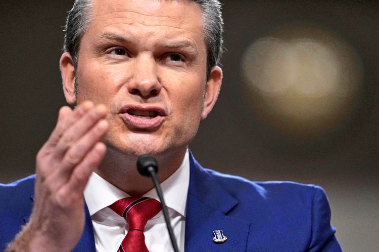 Ein Mann in einem blauen Anzug mit roter Krawatte spricht vor einem Mikrofon während einer Anhörung. Er hebt eine Hand in einer gestikulierenden Bewegung. Der Hintergrund ist unscharf.