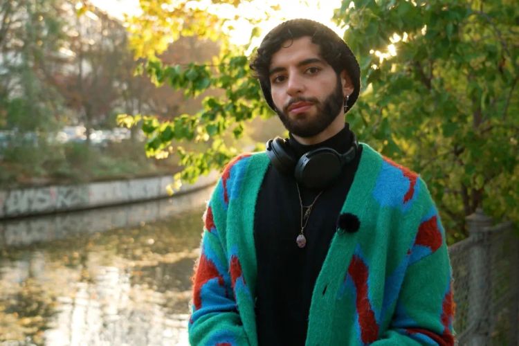 Ahmed, ein junger muslimischer und queerer Mann in einem bunten Cardigan in Berlin. 