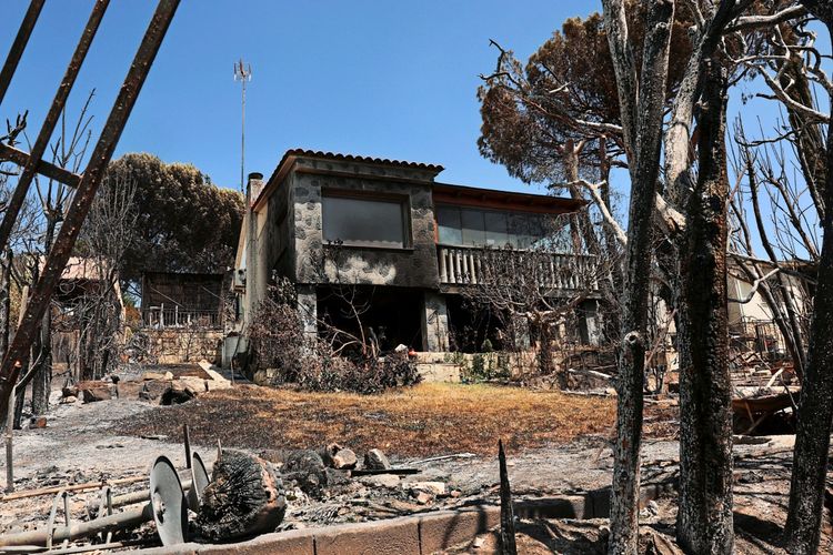 Ein beschädigtes Haus mit verkohlten Bäumen und verbrannter Vegetation in einer von Waldbränden betroffenen Gegend in El Encinar del Alberche, Toledo, Spanien. Himmel ist klar.