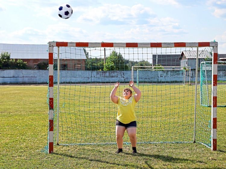 Übergewichtiges Mädchen steht auf einem Fußballplatz im Tor und versucht einen Ball zu halten 