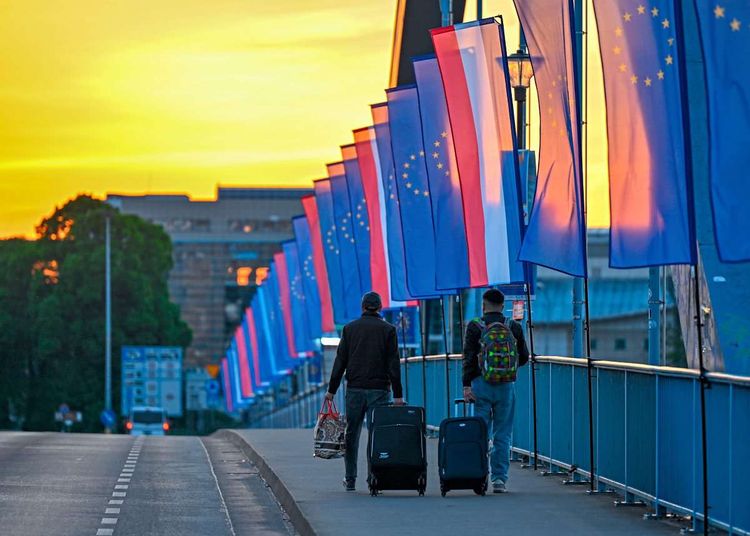 Zwei Männer mit Rollkoffer und Rucksack gehen über die mit EU-Flaggen und Länderflaggen dekorierte Stadtbrücke über den Grenzfluss Oder zwischen Frankfurt an der Oder und dem polnischen Slubice.
