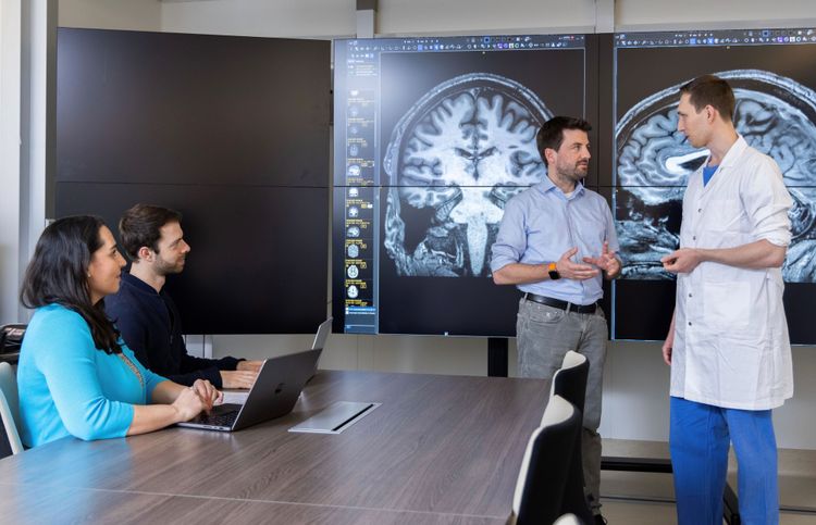 Georg Langs steht mit einem Kollegen vor einem Scan eines Gehirns, auf einem Tisch daneben sitzen zwei Personen mit Laptops
