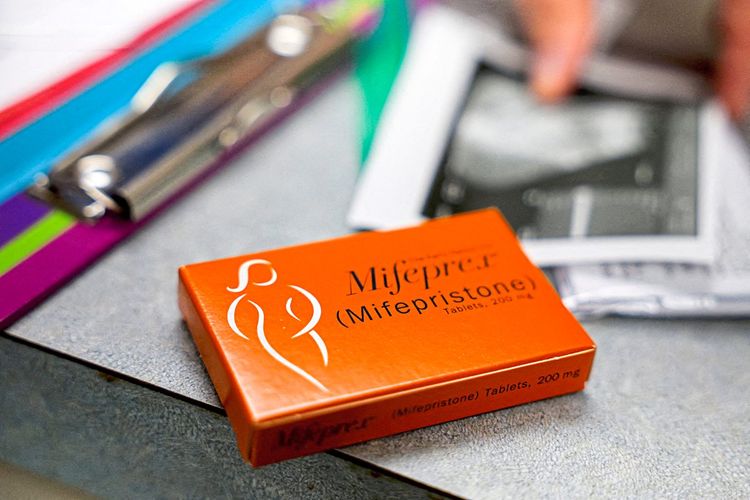 Eine Packung der Abtreibungspille Mifepristone liegt auf einem Tisch. Daneben ein Ordner mit Unterlagen und ein verschwommenes Ultraschallbild. 