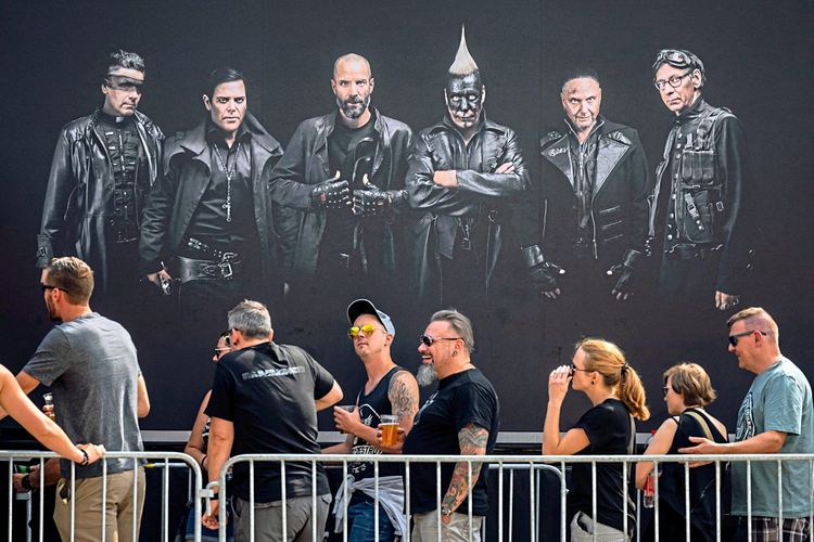 Weibliche und männliche Fans stehen vor einem Rammstein-Plakat, auf den Einlass zum Konzert wartend