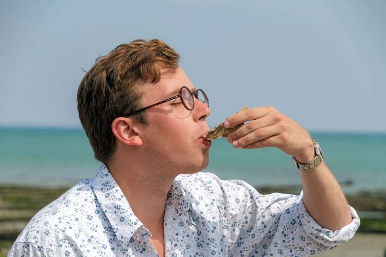 Junger Mann schlürft eine Auster