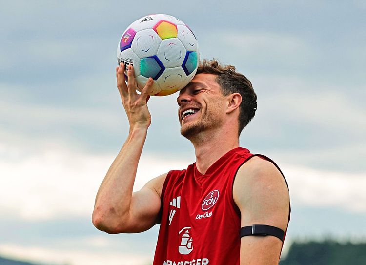 Ein lachender Fußballer hält sich einen Fußball an den Kopf