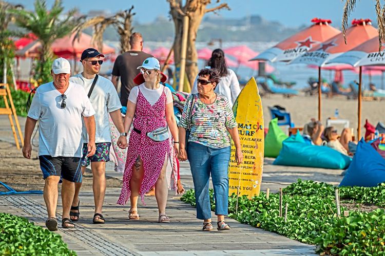 Touristen spazieren über einen Strand auf Bali.
