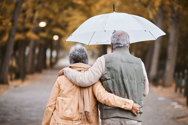 Ein älteres Paar gehen unterm Regenschirm durch eine Allee